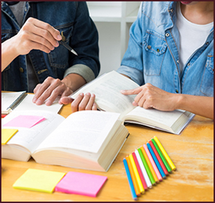 Two students working together at a desk with books and colored pencils