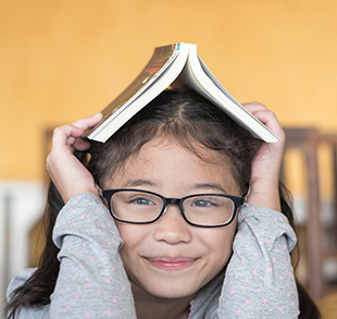 Smiling young girl with folding book on head