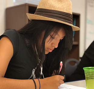 High school girl with hat focusing on writing assignment